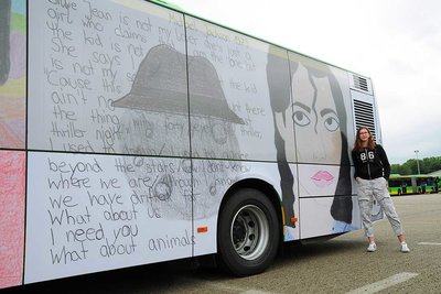 A girl is standing at the back of a STOAG bus that has the winning motif of the 2020 creative competition printed on it