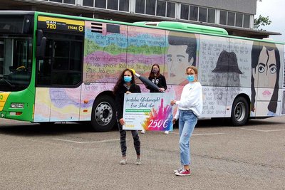 Three schoolgirls stand in front of a printed STOAG bus and check the winnings for the 2020 creative competition