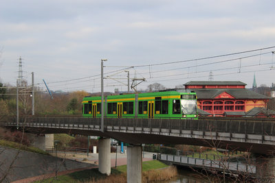 A STOAG tram drives over a bridge, with a red building in the background