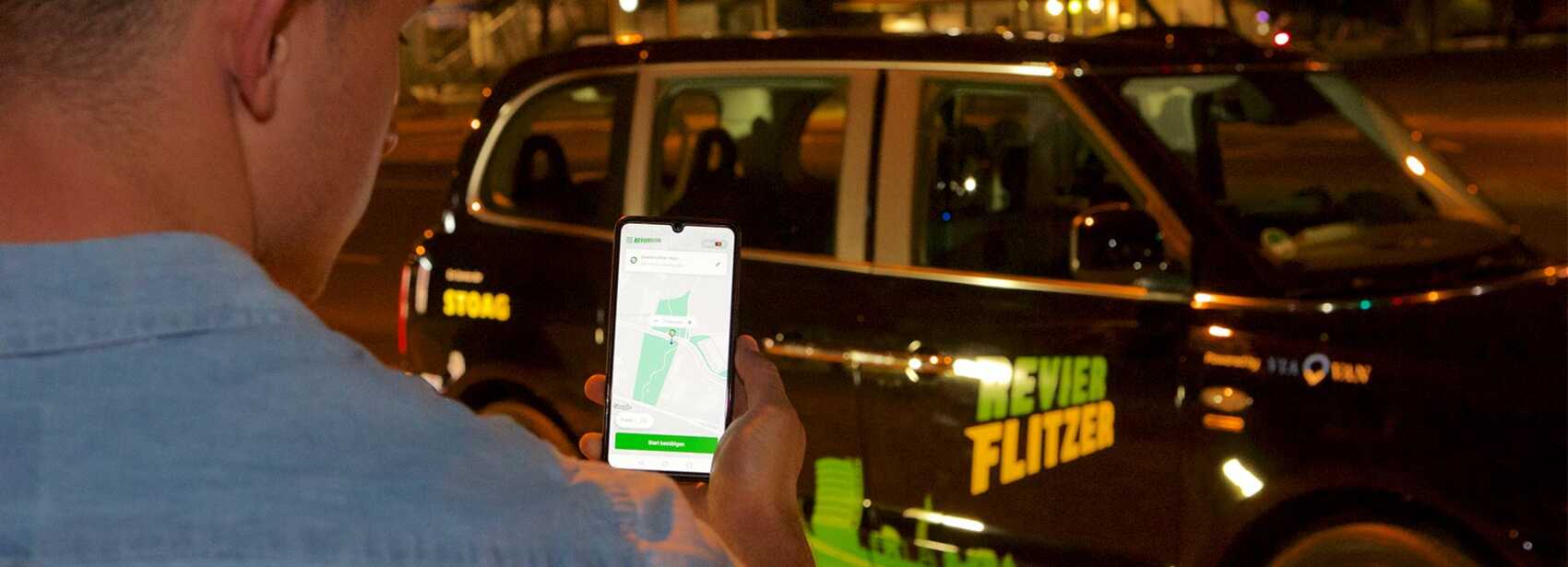 Person schaut auf Smartphone vor dem Revierflitzer der STOAG