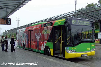A STOAG vehicle with SC Rot-Weiß advertising is parked at a bus station with people waiting