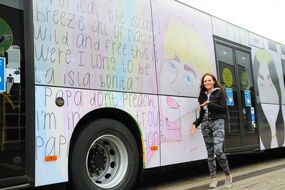 A schoolgirl is standing in front of a bus with the winning motif of the 2020 creative competition printed on it